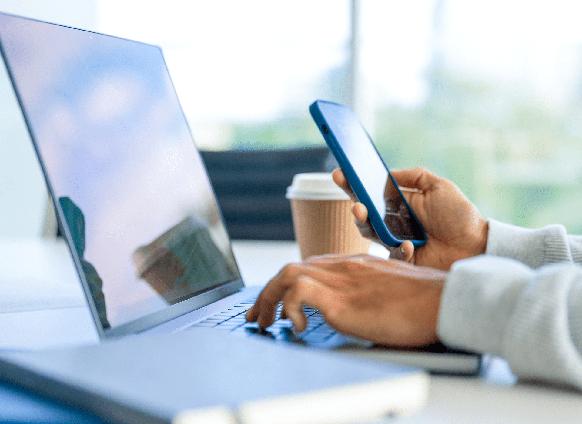 Hands holding phone, typing on laptop