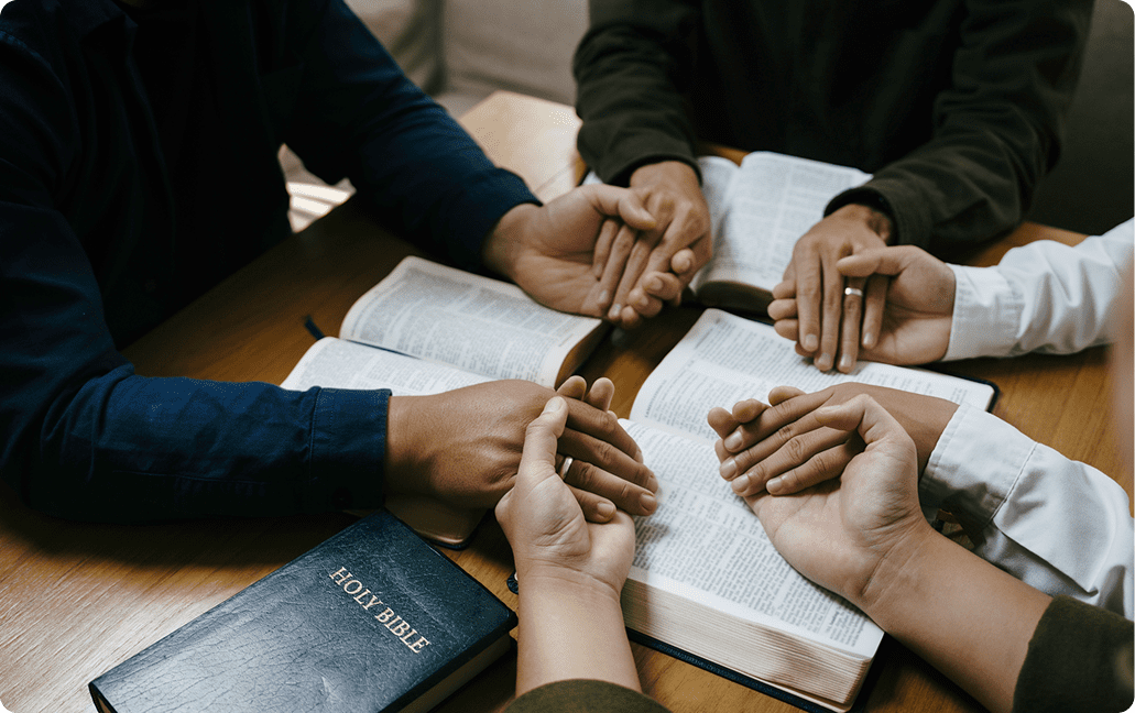 Hands holding in prayer over open Bibles